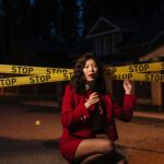 Female reporter at a crime scene with stop tape, crouching and holding a microphone at night.